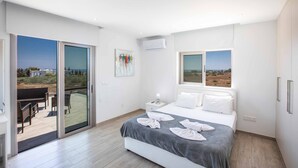 A modern bedroom with a large bed, a sliding glass door to an outdoor area, and a view of the landscape. - Villa Demeter GA98 - Six Bedroom Villa, Sleeps 12 (Paralimni)