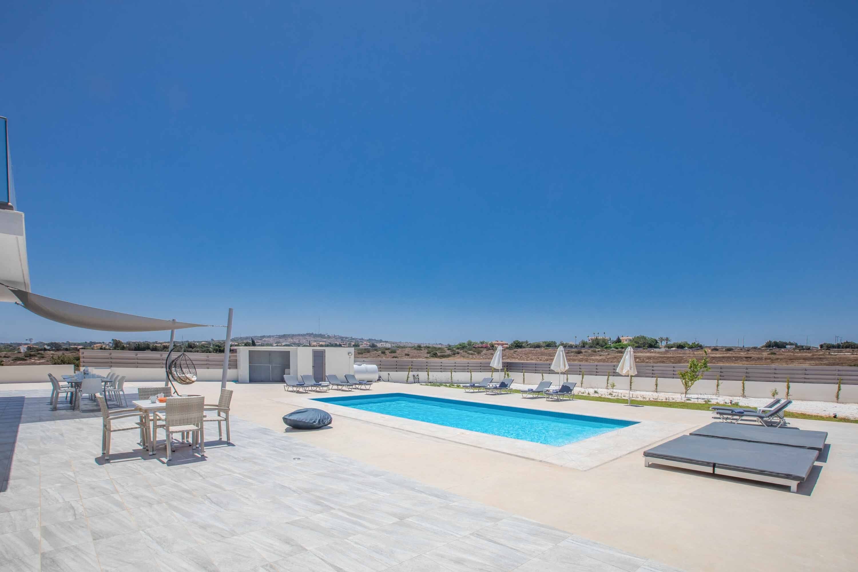 A rooftop pool area with lounge chairs and a table, surrounded by a clear sky and distant landscape.
