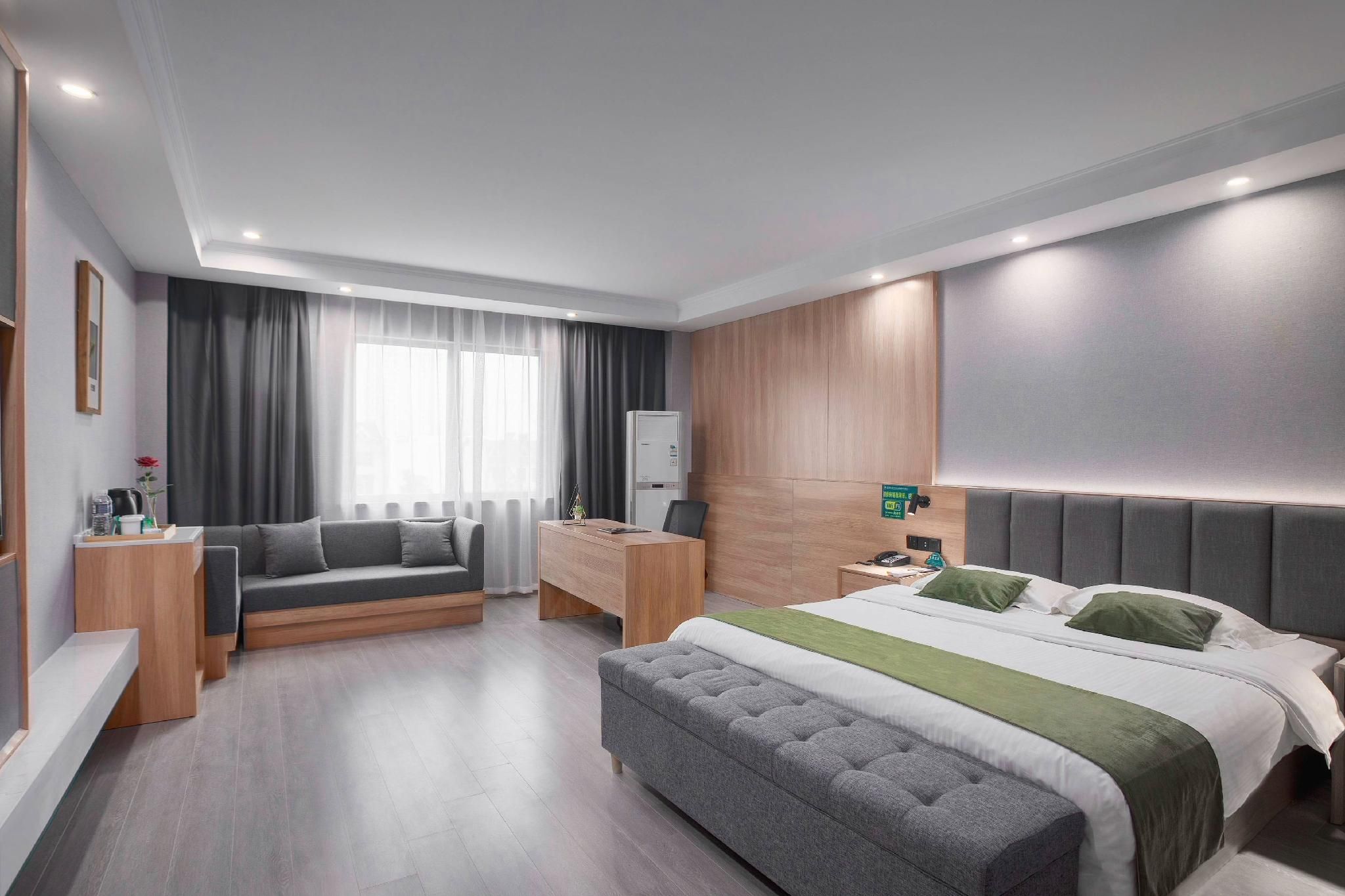A modern hotel room with a bed, a sofa, a desk, and a wardrobe.