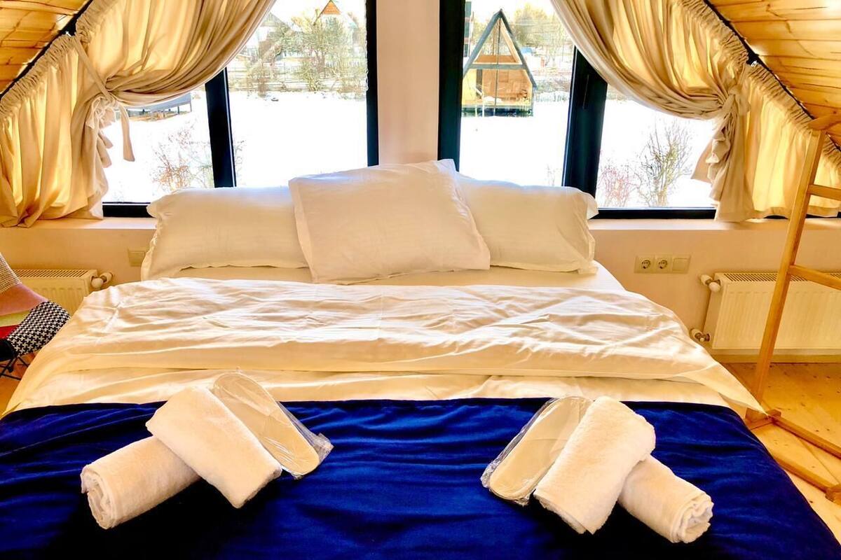 A neatly made bed with white linens and two towels on a blue bedspread, with a view of a building outside through large windows.