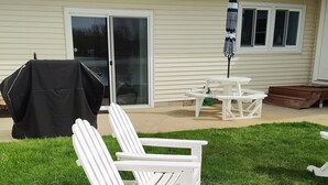 Un jardin avec un barbecue couvert, deux fauteuils Adirondack, une table de pique-nique et un parasol de patio.