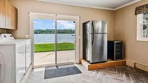 Une cuisine équipée d’un réfrigérateur en acier inoxydable, d’un lave-linge et offrant une vue sur un lac grâce à une porte-fenêtre coulissante.