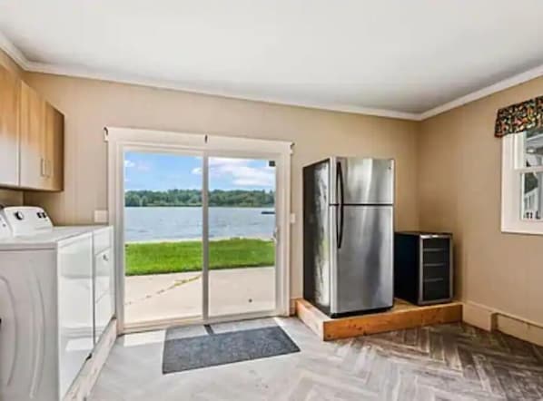 A kitchen with a stainless steel refrigerator, a washing machine, and a view of a lake through a sliding glass door.