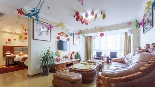 A spacious living room with a large brown leather sofa, a flat-screen TV mounted on the wall, and a dining area with a table and chairs. - Greentree Alliance Laizhou Bus Station Wenhua West Street (Yantai)