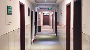 Un couloir d’hôtel avec un sol recouvert de moquette, des portes des deux côtés et un extincteur sur le côté gauche.