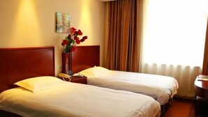 Une chambre d’hôtel avec deux lits simples, une tête de lit en bois, une table de chevet avec une lampe, un vase rempli de fleurs rouges et un tableau accroché au mur.