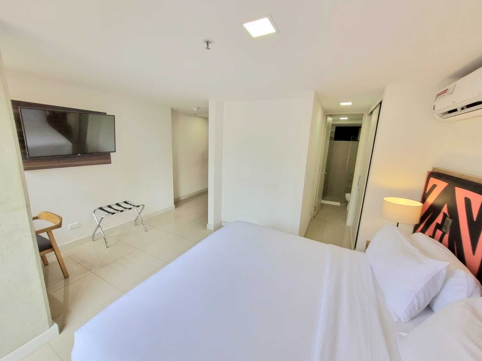 Une chambre d’hôtel équipée d’un lit, d’un téléviseur fixé au mur, d’une chaise, d’un porte-serviettes et d’un appareil de climatisation.