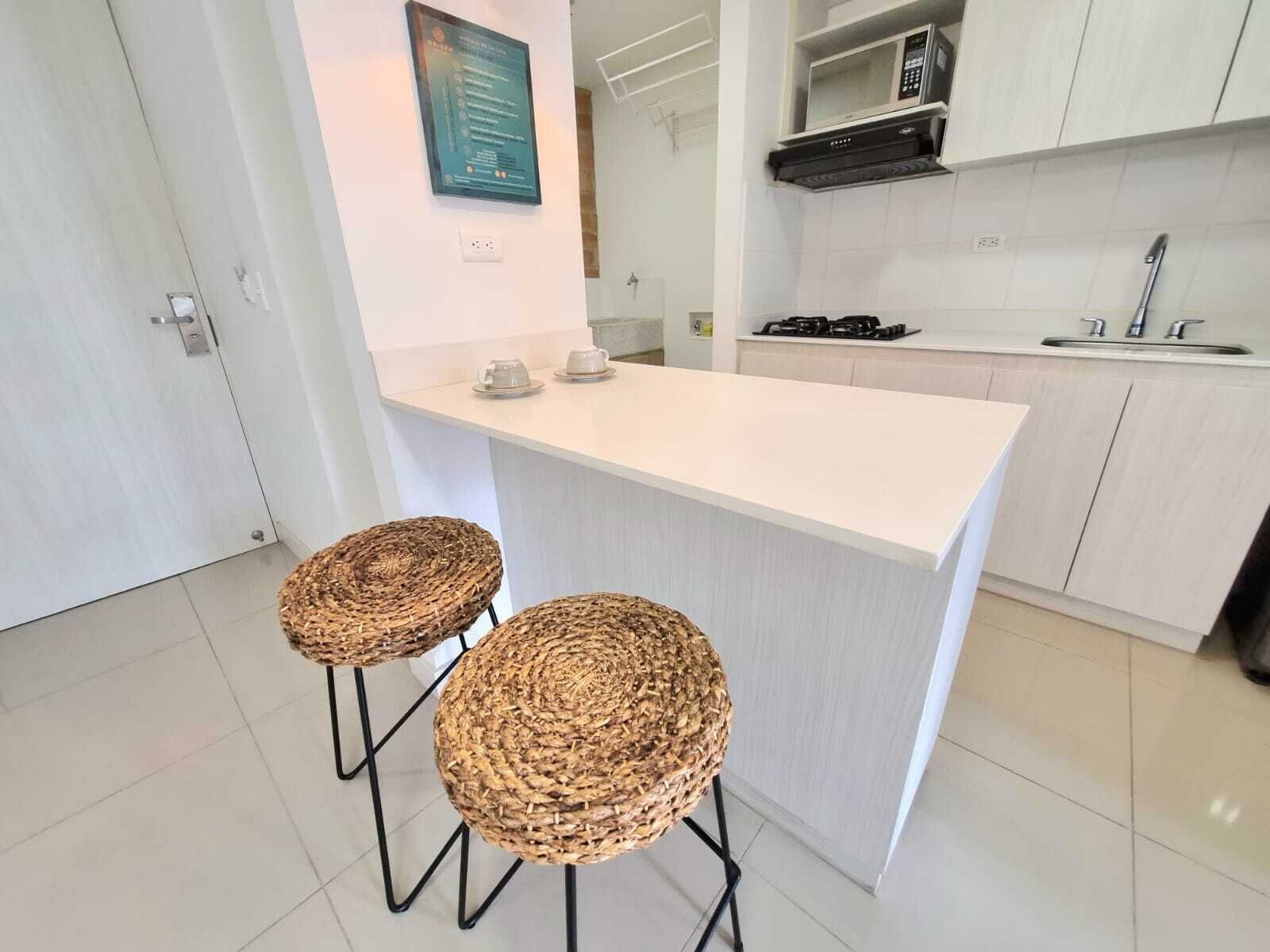 A modern kitchen with a white countertop, two wicker stools, a microwave, and a gas stove.