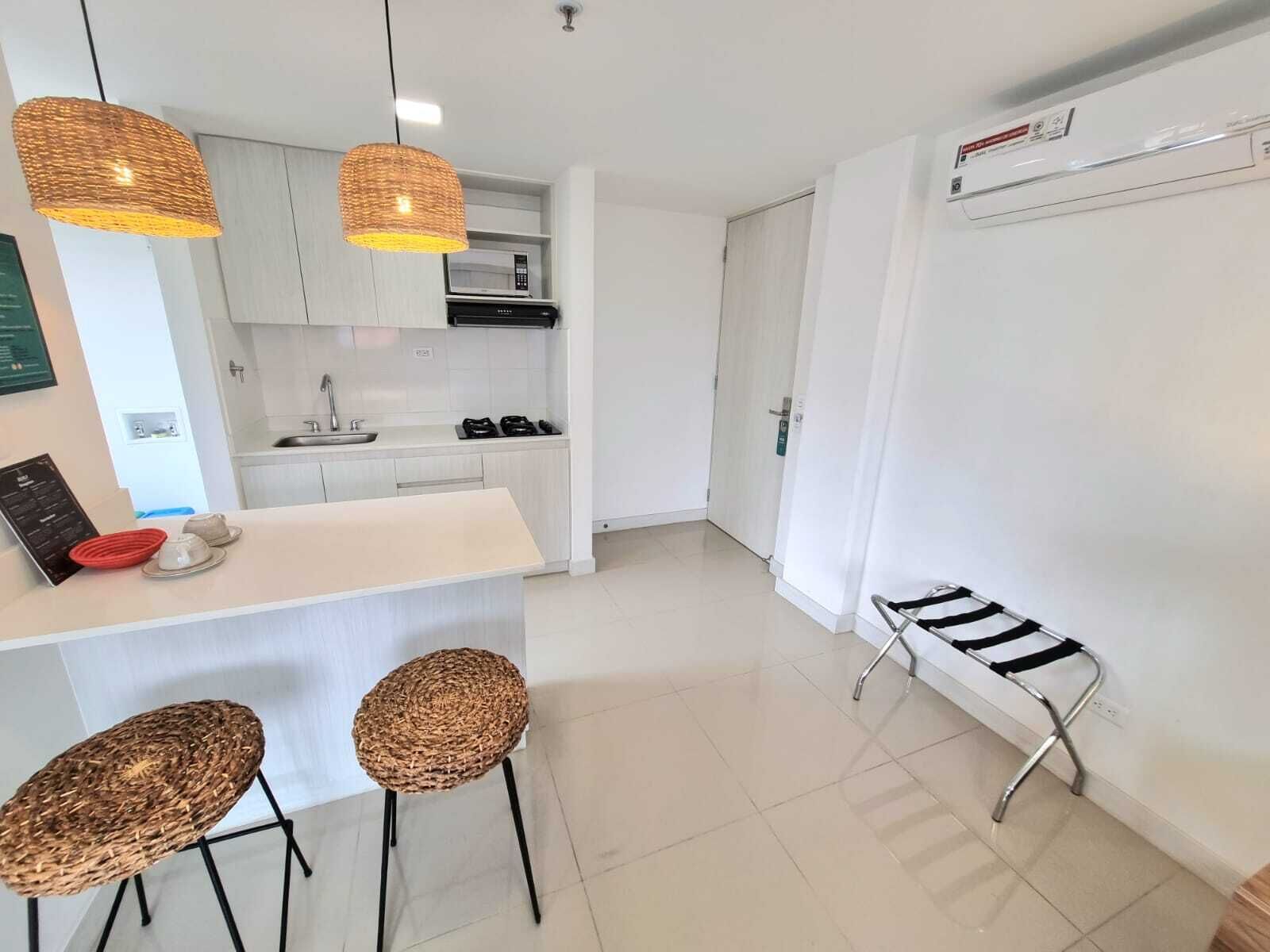 A modern kitchen with white cabinets, a central island, two wicker chairs, and pendant lights.