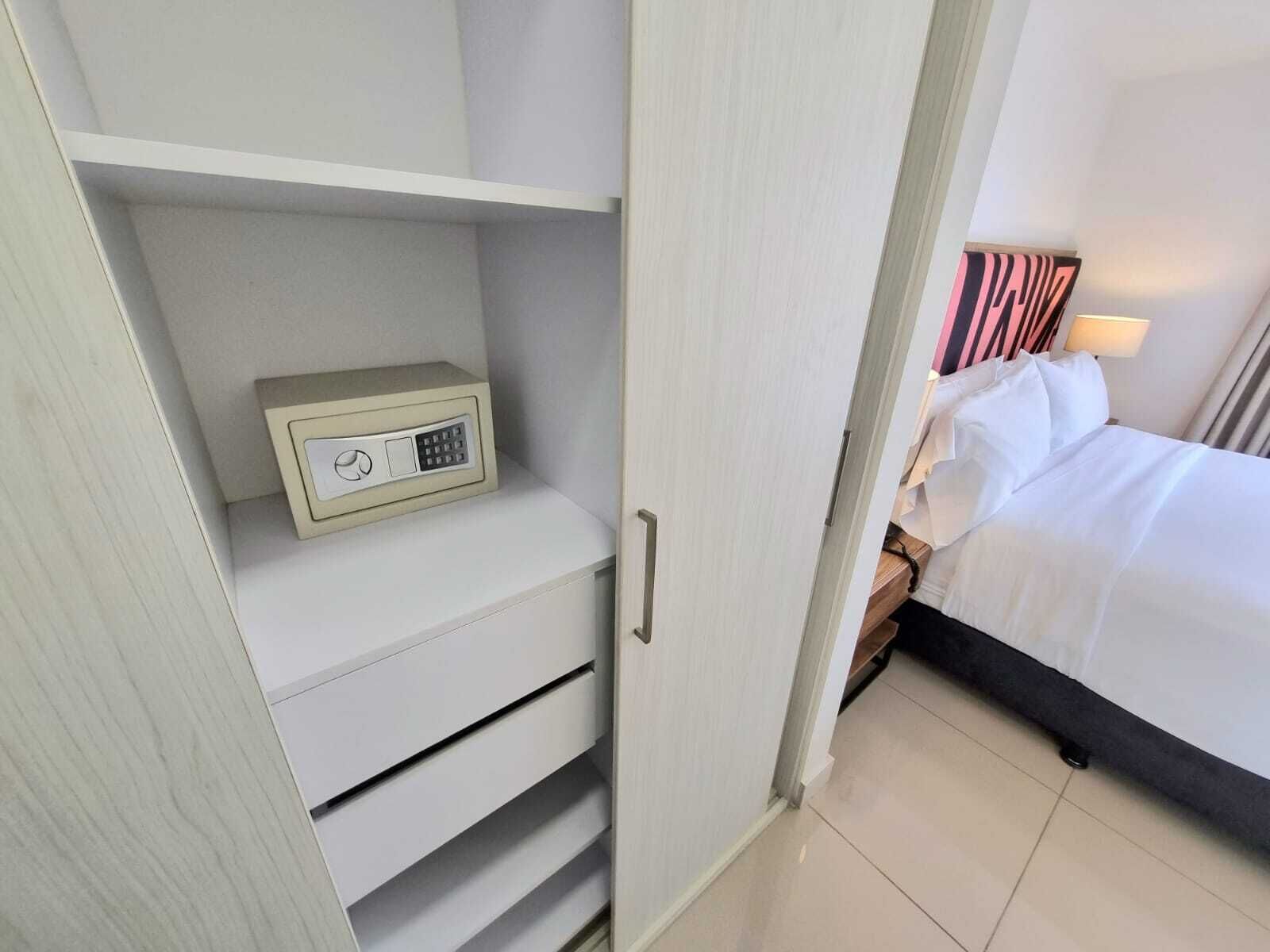 A hotel room with a bed, a nightstand, a lamp, a wardrobe, and a safe.