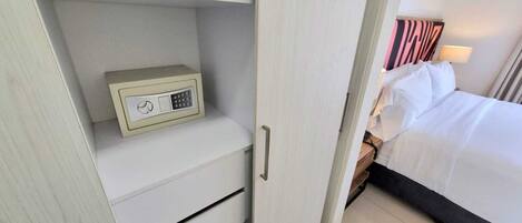 Una habitación de hotel con cama, mesita de noche, lámpara, armario y caja fuerte.