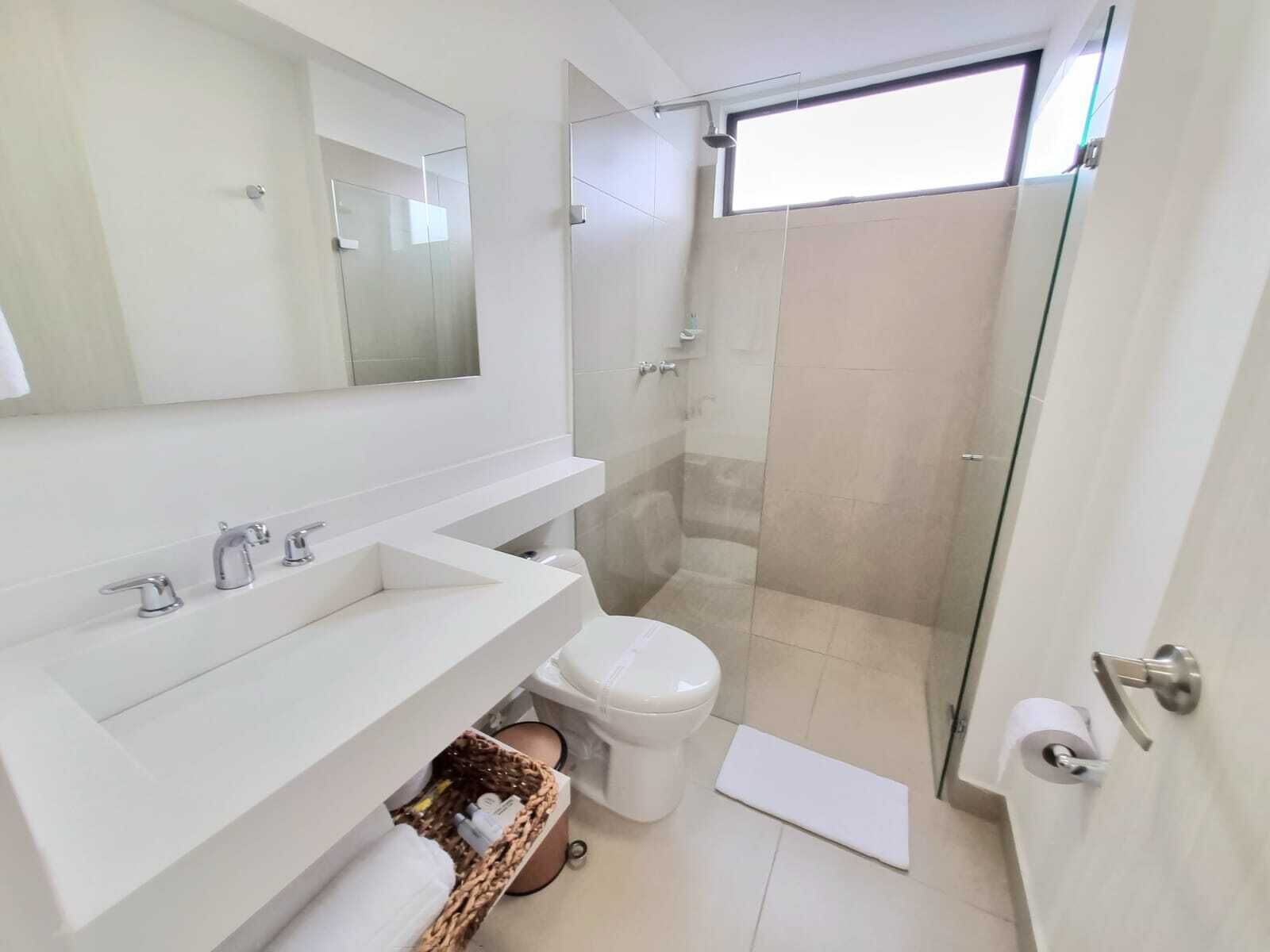 Een moderne badkamer met een glazen douchecabine, een witte wastafel met een spiegel erboven en een toilet met een rol wc-papier op de vloer.