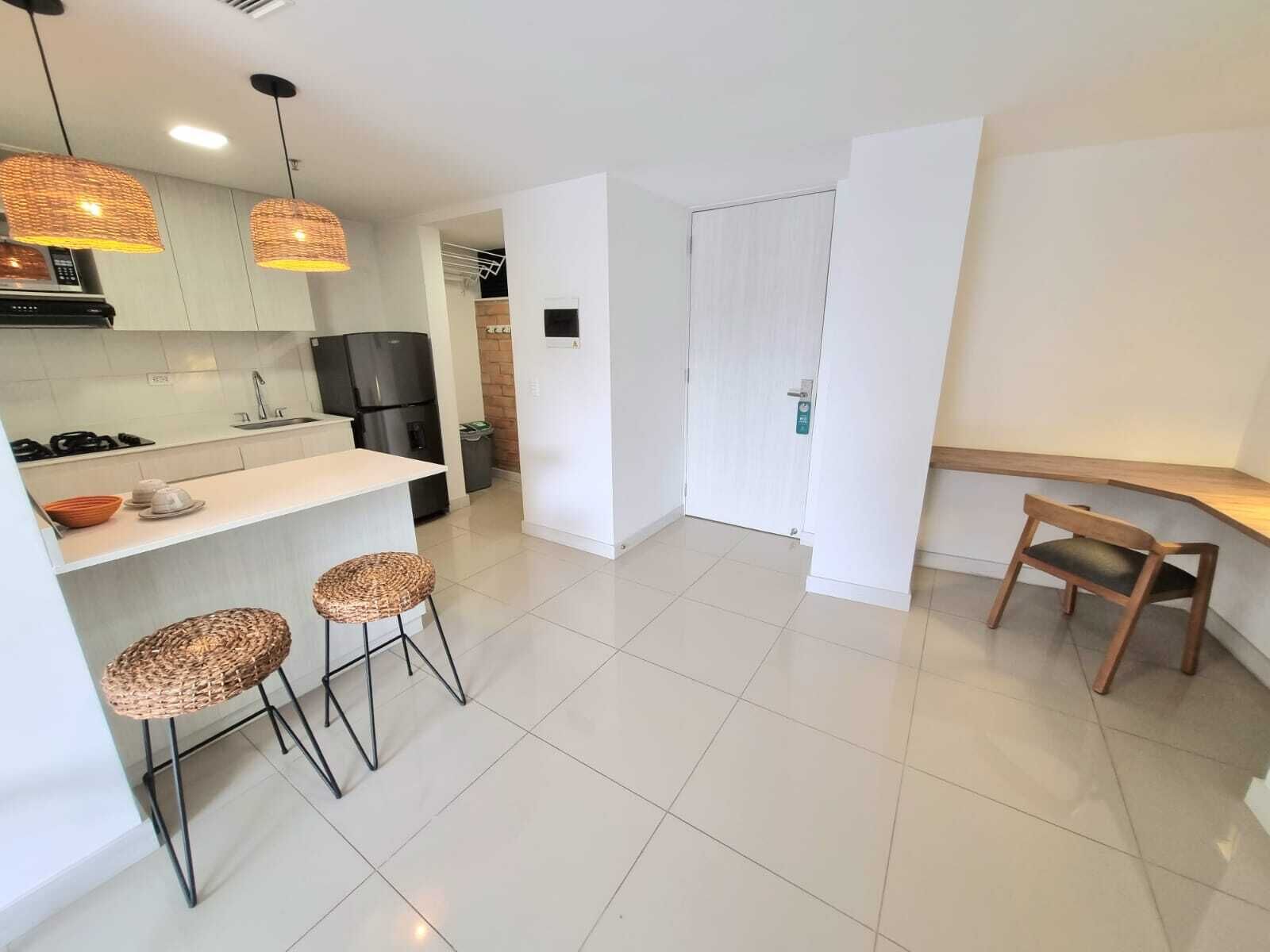 A modern kitchen with white cabinets, a black refrigerator, and a dining area with two wicker stools and a wooden chair.