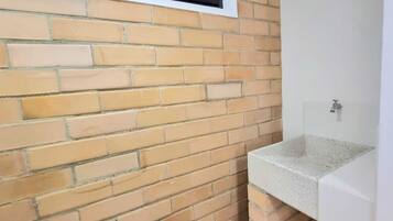 Um banheiro com parede revestida de azulejos, janela com ventilação e pia branca.