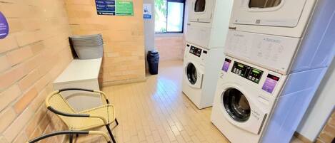 A laundry area with stacked washing machines, a bench, and wicker chairs.