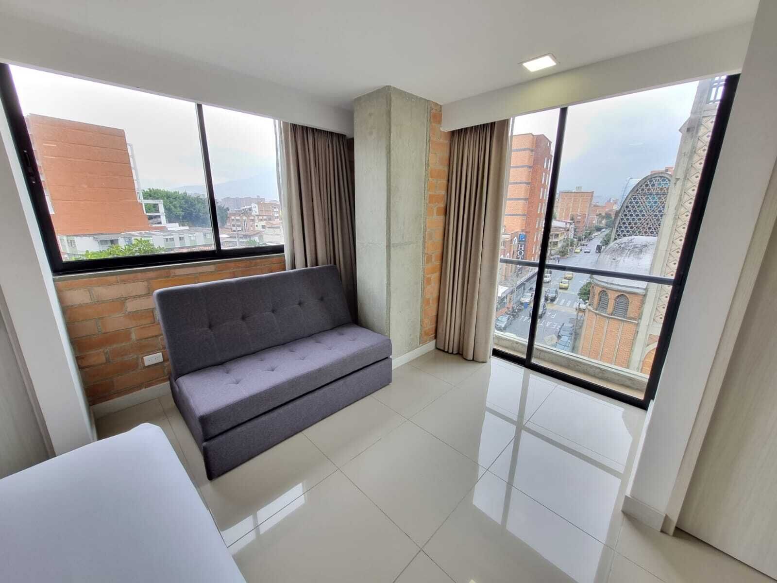 A modern apartment with a grey sofa, large windows, and a view of the cityscape.