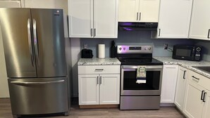 A kitchen with white cabinets, a stainless steel refrigerator, a microwave, a toaster, and a stove. - Family Friendly {5 Min To WSU} Spacious (Wichita)
