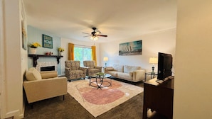 A living room with a sofa, armchairs, a coffee table, a fireplace, a ceiling fan, and a television. - Family Friendly {5 Min To WSU} Spacious (Wichita)