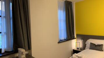 A hotel room with a bed, bedside table, and a window with curtains.