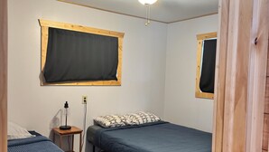 A room with two single beds, a ceiling fan, and a window with a wooden frame. - Charming 2-bedroom cottage with WiFi, AC on quiet lake on trails with kayaks. (Birchwood)