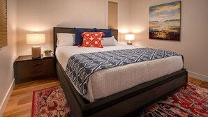 Ein Schlafzimmer mit einem Bett, zwei Nachttischen, einer Lampe, einem Bild und einem gemusterten Teppich.