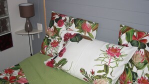 Una camera da letto con un letto, una coperta verde, cuscini a motivi floreali, una lampada da comodino e un comodino con una lampada.