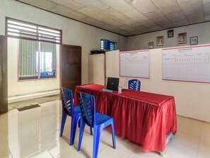 A conference room with a red table, blue chairs, a laptop, and documents on the wall. - OYO Homes 91148 Homesstay Desa Wisata Bahoi (Bahoi)