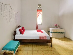 Ein ordentlich eingerichtetes Schlafzimmer mit Bett, Nachttisch, einem kleinen Tisch mit einer Vase und einem Fenster mit Vorhängen.
