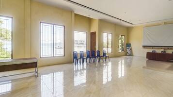 A spacious room with large windows, a wooden bench, and a row of blue chairs.