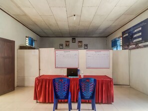 Une pièce comprenant un comptoir d’accueil, deux chaises bleues, un ordinateur portable et deux grandes affiches au mur.