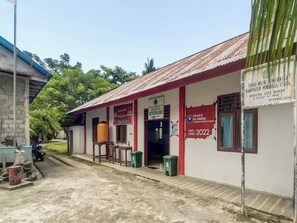 A building with a corrugated metal roof, a signboard, and a trash bin. - OYO Homes 91148 Homesstay Desa Wisata Bahoi (Bahoi)