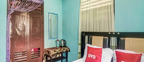 A room with a bed, a wooden wardrobe, a small table with a kettle, and a mirror on the wall.