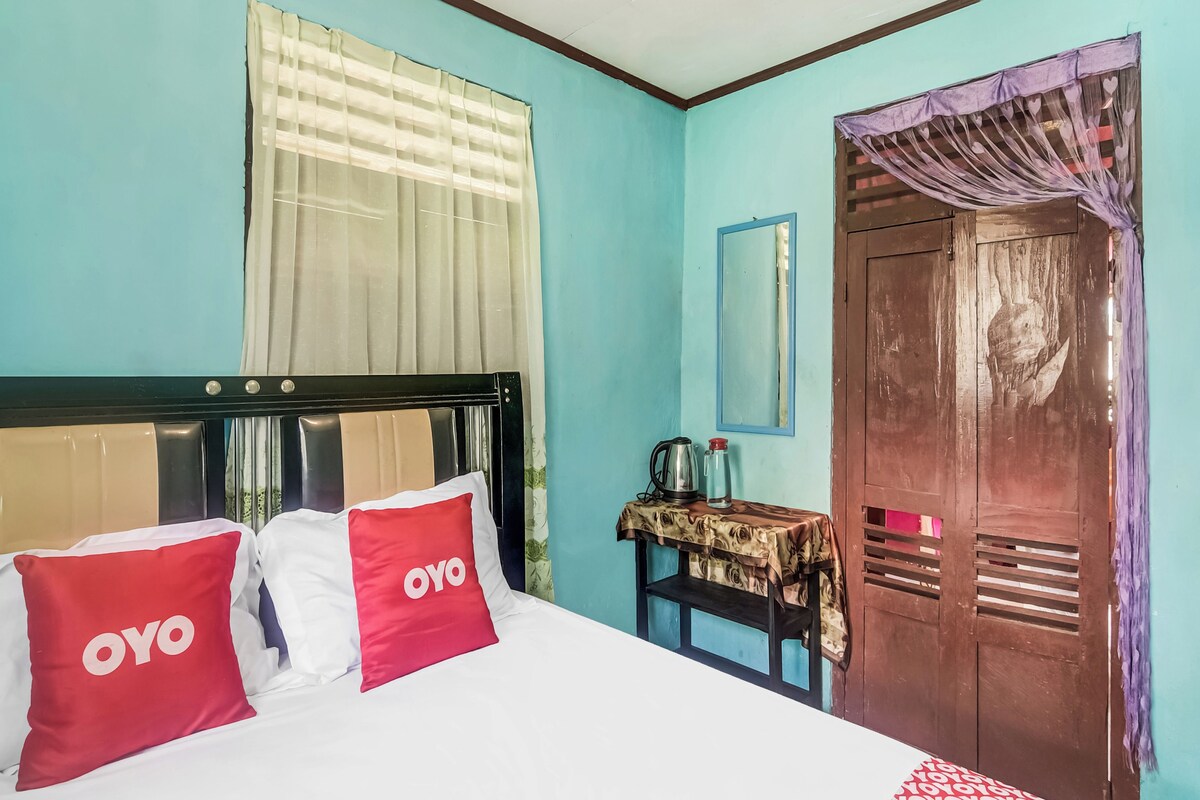 Ein Zimmer mit einem Bett, einer Holztür, einem kleinen Tisch mit Wasserkocher und einem Spiegel an der Wand.