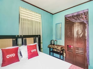 Une pièce avec un lit, une porte en bois, une petite table avec une bouilloire et un miroir au mur.
