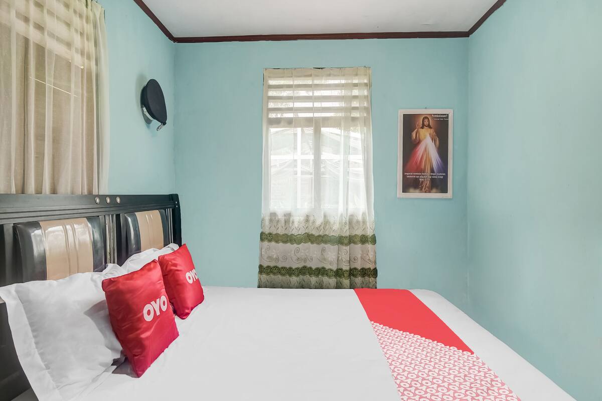 Un dormitorio con cama, ventana con cortinas, un cartel en la pared y cabecero.