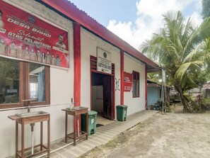 Un edificio con techo rojo, un letrero y un bote de basura verde en el exterior.