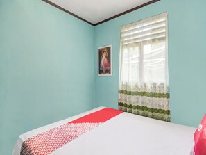 Un dormitorio con una cama individual, una ventana con cortinas translúcidas y un cartel en la pared.