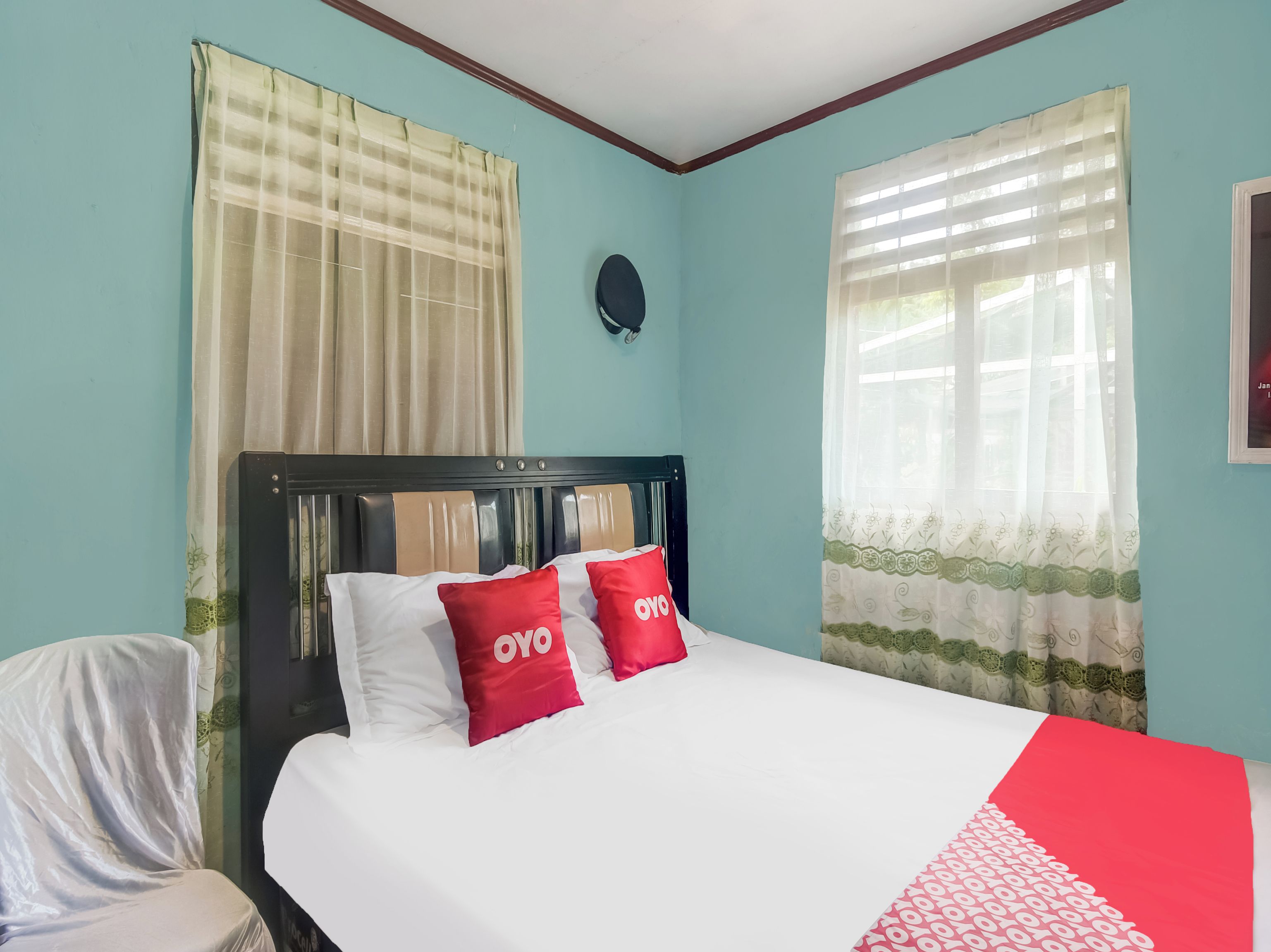 A hotel room with a bed, curtains, a headboard, and a wall clock.