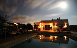 Un edificio con piscina, zona de estar al aire libre y cielo iluminado por la luna.