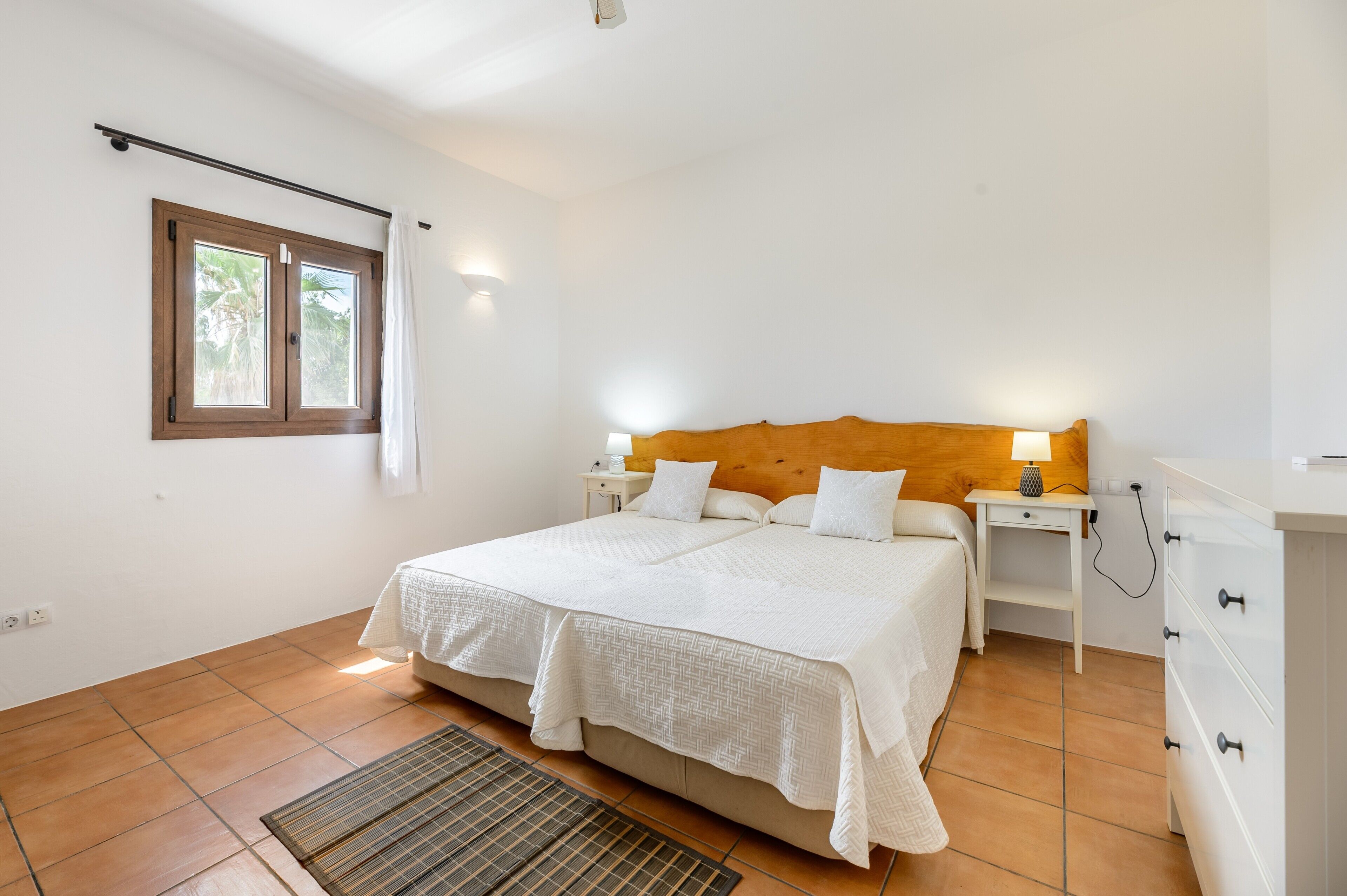 Une chambre à coucher avec un lit, des tables de chevet, une lampe, une fenêtre et une tête de lit en bois.