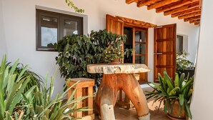 Uma mesa de madeira com um vaso grande e uma planta, rodeada por outros vasos diversos e um banco de madeira.