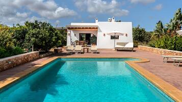 Un espace piscine avec une piscine à l’eau cristalline, un bâtiment blanc doté d’une terrasse et des meubles d’extérieur.