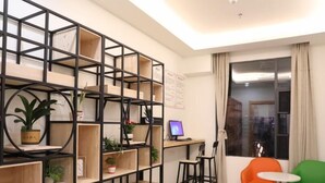 A modern living room with a black metal shelving unit, a small desk with a computer, two chairs, and a large window with curtains. - Greentree Inn Fuzhou Linchuan Yizhong (Fuzhou)