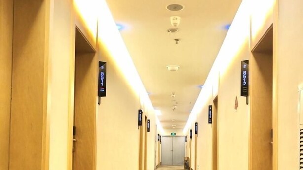 A hotel corridor with doors marked by black signs, a ceiling with recessed lighting, and an emergency exit sign. - Greentree Inn Fuzhou Linchuan Yizhong (Fuzhou)