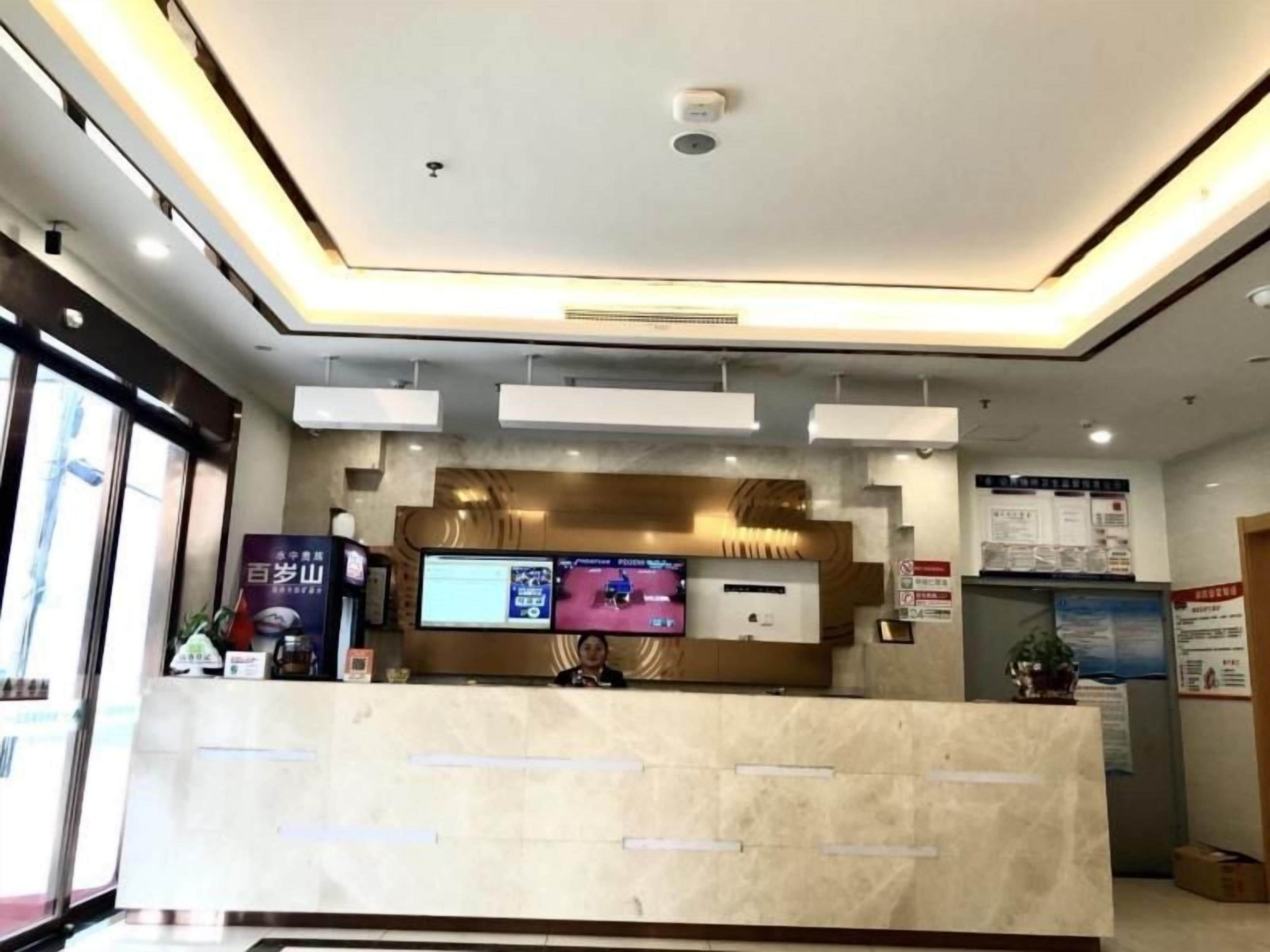 Un espace d’accueil d’hôtel avec un comptoir en marbre, un écran numérique et un panneau d’affichage.