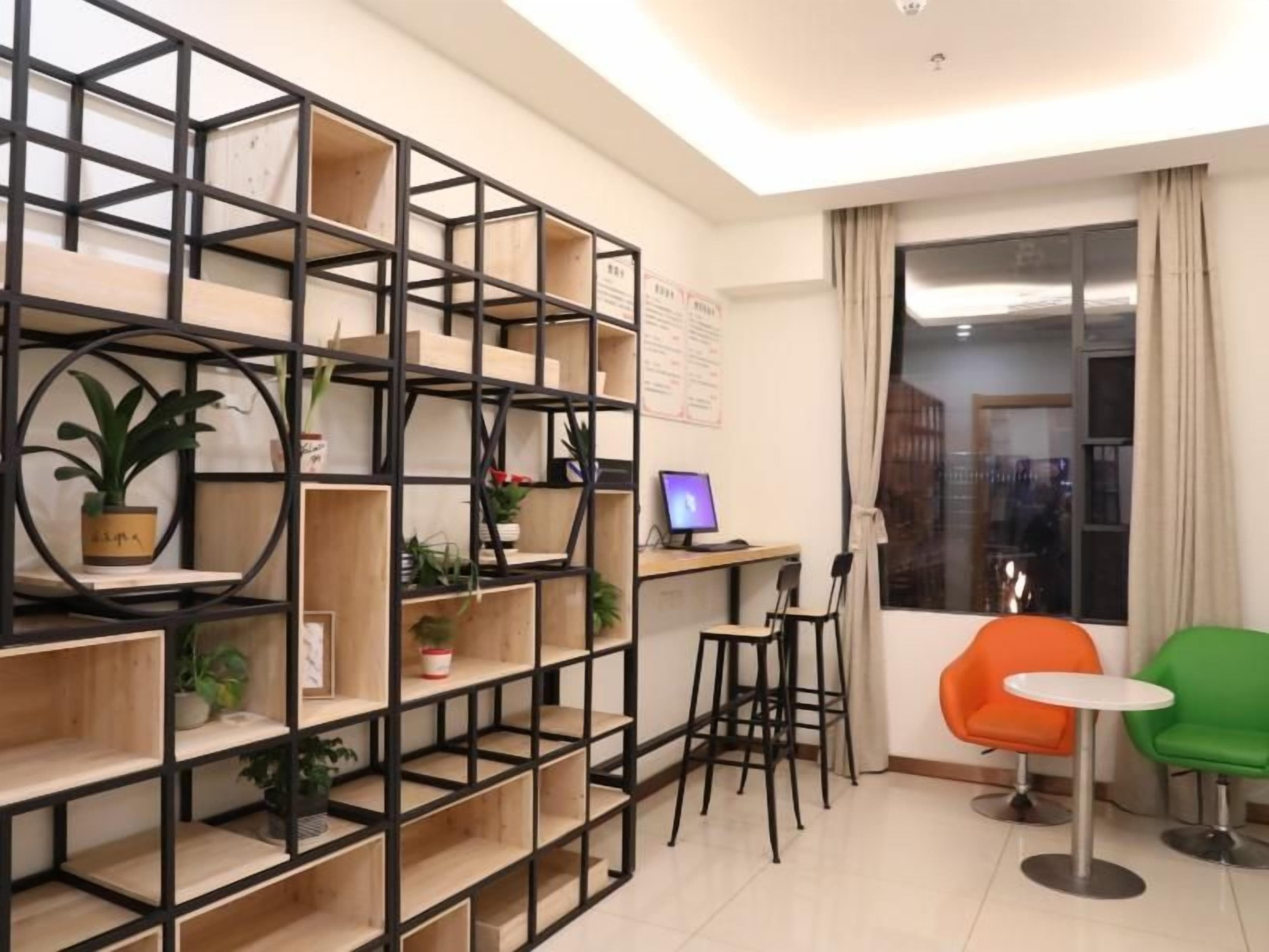A modern living room with a black metal shelving unit, a small desk with a computer, two chairs, and a large window with curtains.