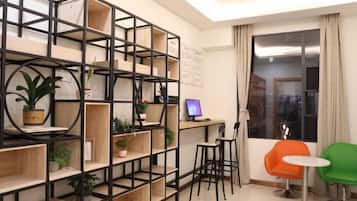 A modern living room with a black metal shelving unit, a small desk with a computer, two chairs, and a large window with curtains.
