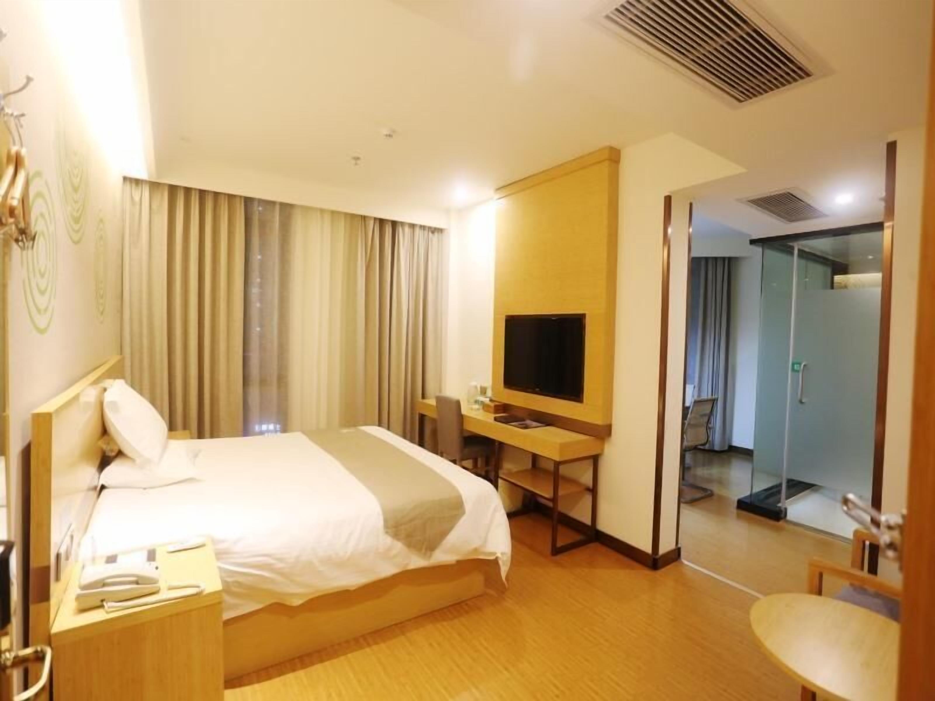 A hotel room with a bed, a desk with a television, a mirror, and a door leading to another room.