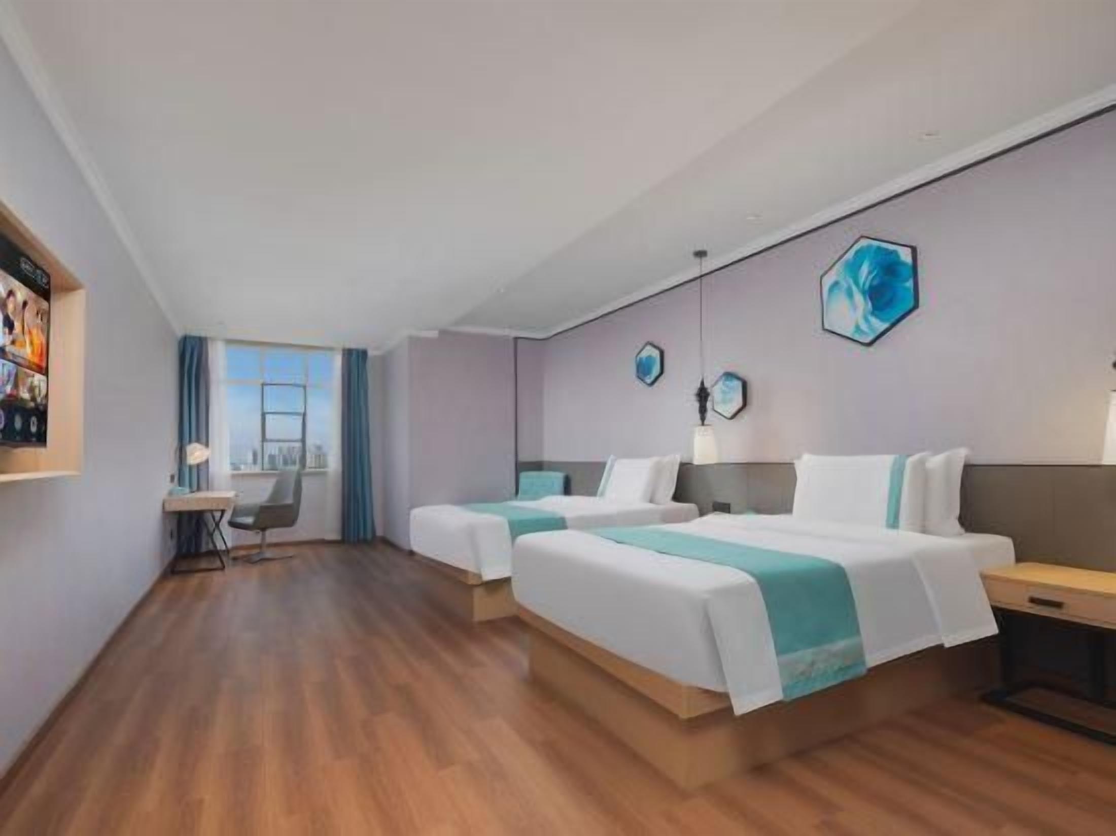 A hotel room with two beds, a desk, and a view of the city.