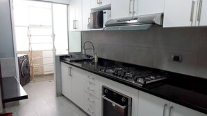 Uma cozinha moderna com armários brancos, uma coifa de aço inoxidável, micro-ondas e lava-louças.